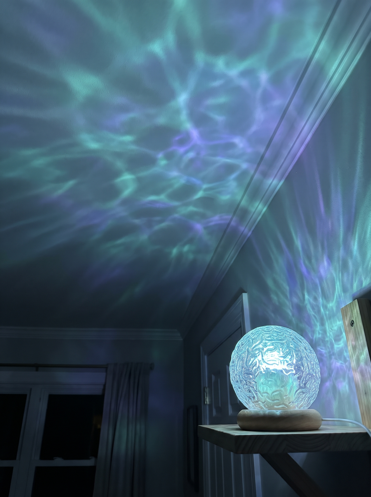 Teal and violet ocean-wave light across a bedroom ceiling from a crystal projector lamp
